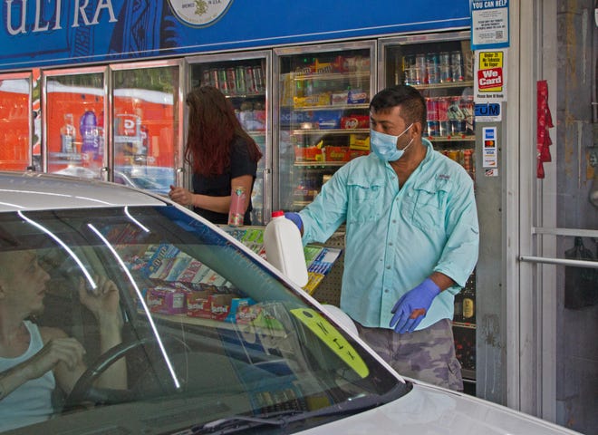 Mamun Aktar wears a protective medical mask and gloves Thursday afternoon as he delivers items to customers at EZ-Way Drive Thru in the Inwood section of Winter Haven. Inwood lies within zip code 33881, which has produced the highest total of COVID-19 cases in Polk County. [GARY WHITE/THE LEDGER]