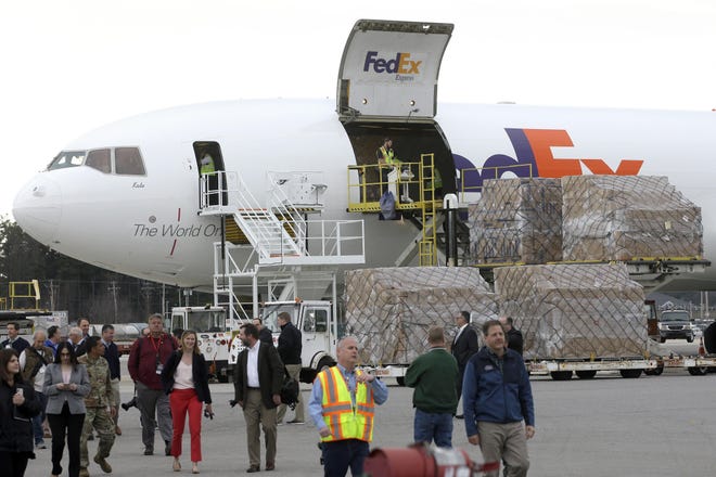 Law enforcement and government officials, along with members of the media, walk along the tarmac as pallets containing personal protective equipment, right, are unloaded from a FedEx cargo plane, Sunday, April 12, 2020, at Manchester-Boston Regional Airport, in Manchester, N.H. The cargo plane, carrying about 91,000 pounds of personal protective equipment, which is helpful in preventing the spread of the coronavirus, arrived at the airport in Manchester from Shanghai, China, after passing through U.S. Customs in Anchorage, Alaska early Sunday, April 12. [AP Photo/Steven Senne]