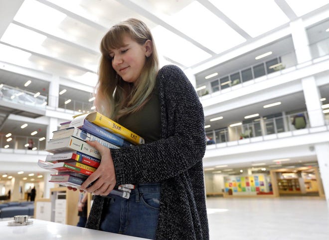 Zoe Abel lifts up her stack of books at the Columbus Metropolitan Library on March 13. Zoe says she usually checks out one or two books at a time but with the closure of the library to begin she opted to get 10 books to help her get through the library closure. [Eric Albrecht/Dispatch]