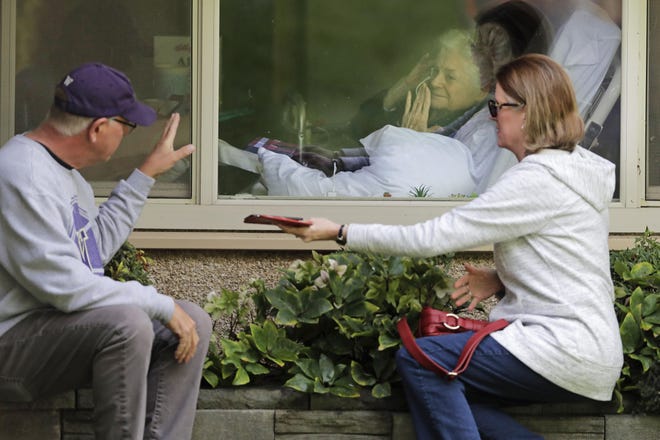 Judie Shape, center, who has tested positive for the coronavirus, blows a kiss to her son-in-law, Michael Spencer, left, as Shape's daughter, Lori Spencer, right, looks on, Wednesday, March 11, 2020, as they visit on the phone and look at each other through a window at the Life Care Center in Kirkland, Wash., near Seattle. In-person visits are not allowed at the nursing home. The vast majority of people recover from the new coronavirus. According to the World Health Organization, most people recover in about two to six weeks, depending on the severity of the illness. (AP Photo/Ted S. Warren)
