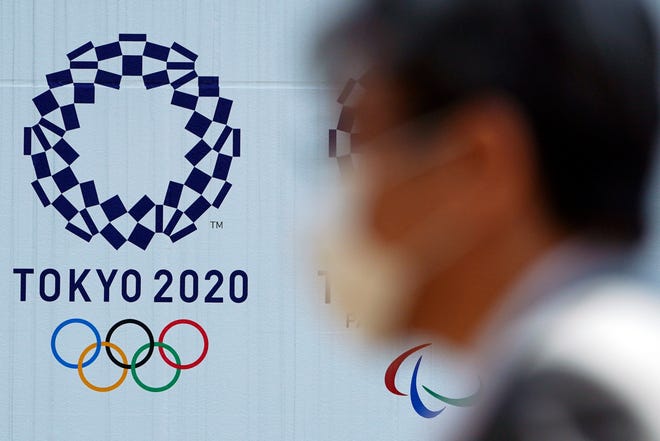 FILE - In this April 2, 2020, file photo, a man wearing a face mask walks near the logo of the Tokyo 2020 Olympics, in Tokyo. Tokyo organizers said Tuesday, April 14, 2020 they have no “B Plan” for again rescheduling the Olympics, which were postponed until next year by the virus pandemic. They say they are going forward under the assumption the Olympics will open on July 23, 2021. (AP Photo/Eugene Hoshiko, File)