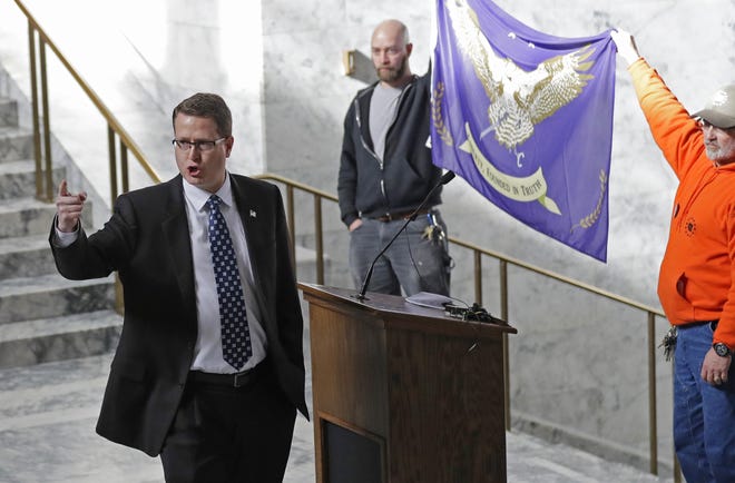FILE - In this Friday, Feb. 15, 2019 file photo, Washington state Rep. Matt Shea, R-Spokane Valley, gestures as he gives a speech in front of the liberty state flag at the Capitol in Olympia, Wash., during a rally held by people advocating splitting Washington state into two separate states and questioning the legality of Washington's I-1639 gun-control measure. Prominent state lawmaker Shea says the coronavirus is a foreign bio-weapon and claims Marxists are using the pandemic to advance totalitarianism. (AP Photo/Ted S. Warren, File)
