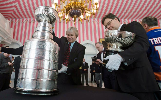 In this March 16, 2017, file photo, Phil Pritchard, left, picks up the Stanley Cup as Craig Campbell, right, holds the original Stanley Cup following an event commemorating the cup's 125th anniversary at Rideau Hall in Ottawa, Ontario. The NHL is on hold, the cup is locked up inside the Hockey Hall of Fame and longtime keeper Pritchard has shed his trademark white gloves to work from home like so many others during the coronavirus pandemic. [Adrian Wyld/The Canadian Press via AP, File]