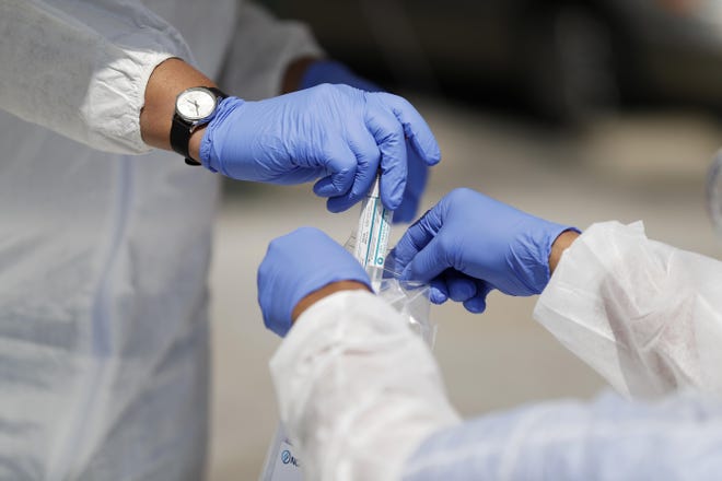 Vials containing nasal swabs collected at a COVID-19 drive-through testing site are dropped into a plastic bag to be sent off for processing after being collected Thursday in St. Louis. [Jeff Roberson/The Associated Press]