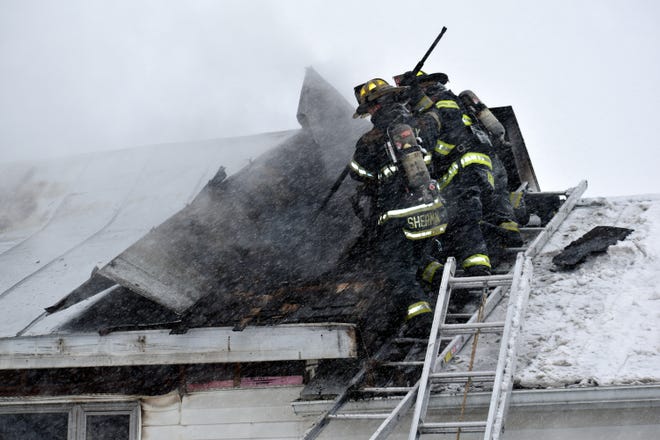 Quincy Fire Chief Mike Sherman and two firefighters tear open the metal roof at 243 Sanford Road in Coldwater Friday morning to get at burning wood and insulation. [Don Reid photo]
