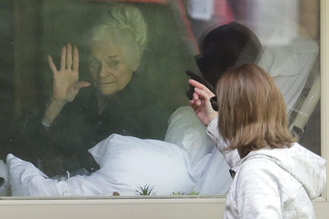 Judie Shape, left, who has tested positive for the coronavirus, waves to her daughter, Lori Spencer, right, Wednesday, March 11, 2020, as they visit on the phone and look at each other through a window at the Life Care Center in Kirkland, Wash., near Seattle. In-person visits are not allowed at the nursing home. The vast majority of people recover from the new coronavirus. According to the World Health Organization, most people recover in about two to six weeks, depending on the severity of the illness. (AP Photo/Ted S. Warren)