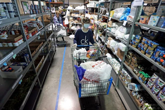 In this April 9, 2020, photo, worker Laura Burbank pushes a cart filled with food for a family through the pantry at GraceWorks Ministries food pantry in Franklin, Tenn. The coronavirus pandemic has provoked a spike in demand for food pantries in the U.S.