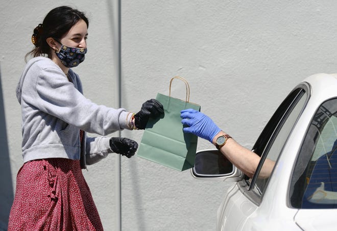 Wearing a protective mask and gloves, budtender Alexi Ezdrin attends to a customer with curbside service Thursday, April 16 at The Higher Path cannabis dispensary in the Sherman Oaks section of Los Angeles. Monday is April 20, or 4/20. That's the code for marijuana’s high holiday, which is usually marked with outdoor festivals and communal smoking sessions. But this year, stay-at-home orders have moved the party online as the marijuana market braces for an economic blow from the coronavirus crisis. (AP Photo/Richard Vogel)