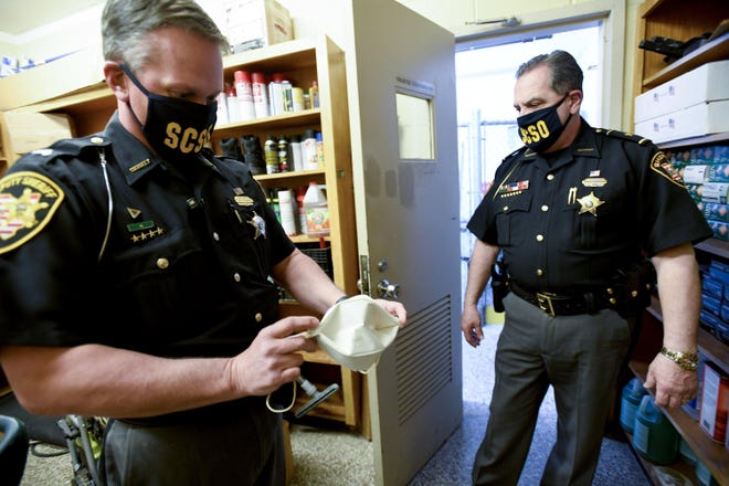 Stark County Sheriff George Sheriff Maier (right) looks on as Sgt. Mike Semen displays a handmade paper face mask that can be used by prisoners at the Stark County Jail, which has implemented numerous safety procedures to combat the threat of COVID-19.