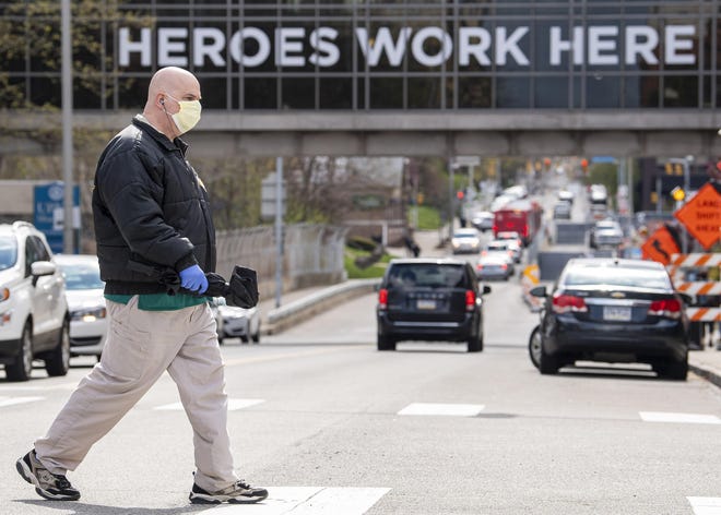 A UPMC Shadyside employee, who declined to give his name, walks to a bus stop near UPMC Shadyside's overpass decorated with signage reading "Heroes work here," during the COVID-19 pandemic Tuesday, April 21, 2020, in Pittsburgh. [STEPH CHAMBERS / PITTSBURG POST-GAZETTE VIA AP]