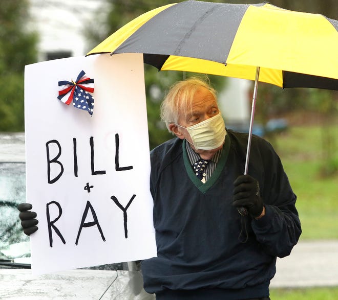 H. Paul Schwitzgebel stands Sunday next to his car in the parking lot of Altercare of Alliance, holding a sign remembering William "Bill" Stanley and Ray Hopson, two of the 15 Altercare patients who died from COVID-19.