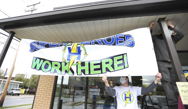 To honor and recognize his employees as Super Heroes Pharmacist Bruce Lefkowitz assist putting up a banner with help from Simon Lezama, right, at Harrold's Pharmacy in Wilkes-Barre on Monday. [MARK MORAN / CITIZENS VOICE VIA AP]