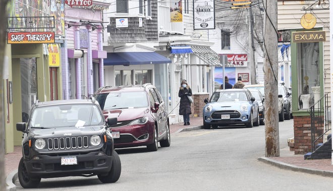 A woman wearing a mask walks her dog along Commercial Street in Provincetown. Pedestrians and bicyclists along a mile-long stretch of the downtown area will be required to wear masks beginning on May 1, as will employees and customers of essential businesses. [Ron Schloerb/Cape Cod Times file]
