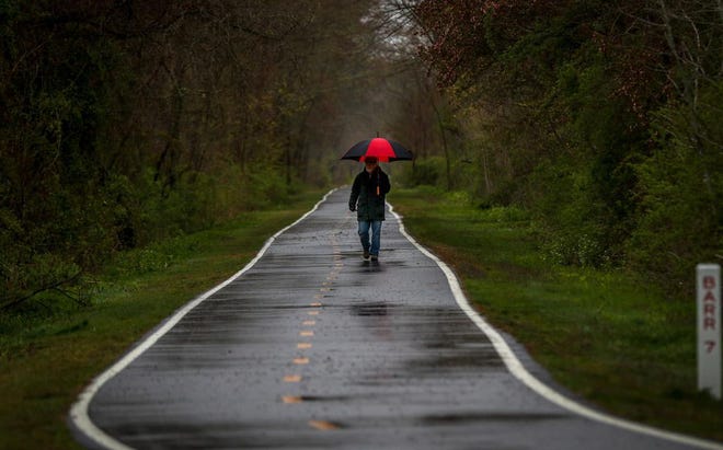 With an umbrella to stop the rain, a walker strolls the bike path Monday near Brickyard Pond in Barrington. Monday’s weather set a new mark in Providence for a record low high temperature. [The Providence Journal / David DelPoio]