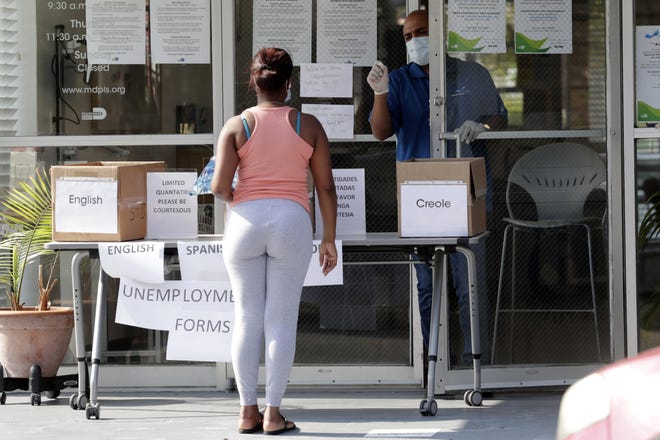 In this Wednesday, April 8, 2020 photo, Harry Varela, right, wears a protective mask as he talks with a woman requesting an unemployment form at a Miami-Dade County library during the new coronavirus pandemic in Miami. [AP Photo/Lynne Sladky]