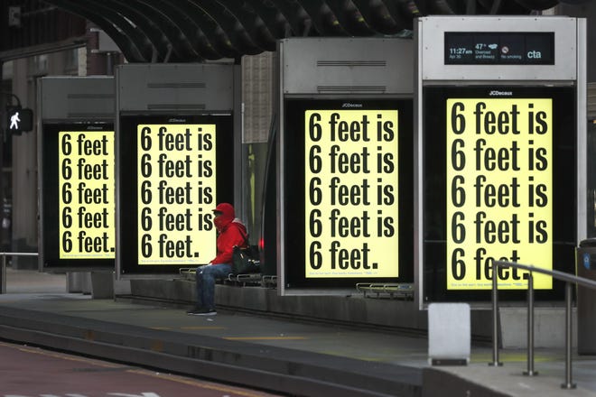 A pedestrian waits for a Chicago Transit Authority bus as several COVID-19 public service messages are projected on screens at the bus stop Thursday in Chicago. [AP Photo/Charles Rex Arbogast]