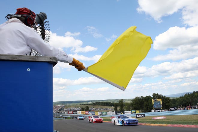 FILE - In this Aug. 6, 2016, file photo, a track marshall waves a yellow caution flag during a NASCAR Xfinity series auto race at Watkins Glen International in Watkins Glen, N.Y. As NASCAR speeds back to the race track during the coronavirus pandemic the series has a heavy responsibility to set a safety standard that doesn't slow the return of other sports. (AP Photo/Mel Evans, File)