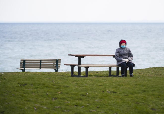 A elderly woman sits alone with Lake Ontario in the background in Toronto, Monday, April 27, 2020. Health officials and the government have asked that people stay inside to help curb the spread of COVID-19. (Nathan Denette/The Canadian Press via AP)