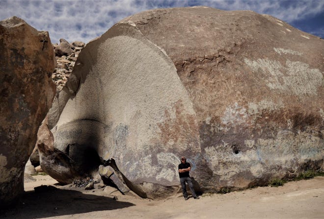 Columnist John R. Beyer poses next to Giant Rock in Landers. The boulder was the largest free-standing boulder in the world until about 20 years ago when the section at left split away. [PHOTO COURTESY OF JOHN R. BEYER]