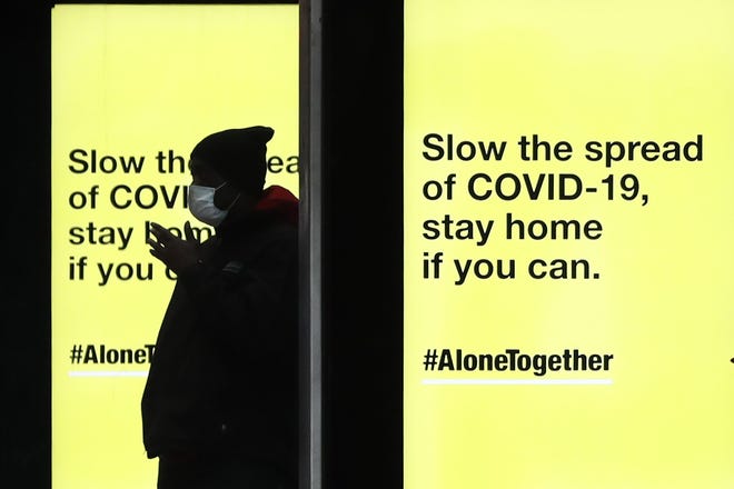 A pedestrian waits in silhouette for a Chicago Transit Authority bus as several COVID-19 public service messages are projected on screens at the bus stop Thursday, April 30, 2020, in Chicago. [CHARLES REX ARBOGAST/THE ASSOCIATED PRESS]