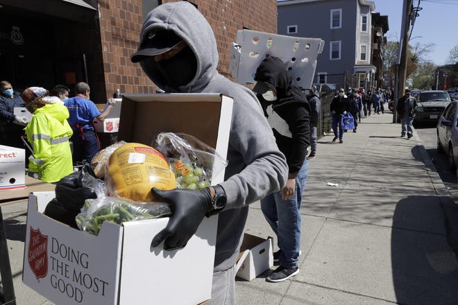 A person wearing mask and gloves out of concern for the coronavirus carries a box of donated food away from a Salvation Army food pantry. [AP Photo]