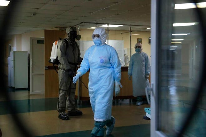 A serviceman of Belarus Ministry of Defence, left, and medical workers wearing protective gear are seen at a local hospital in Minsk, Belarus, Tuesday, May 5, 2020. Despite the World Health Organization's call for Belarus to ban public events as coronavirus cases rise sharply, President Alexander Lukashenko says the country will go ahead with a parade to mark the 75th anniversary of the defeat of Nazi Germany.