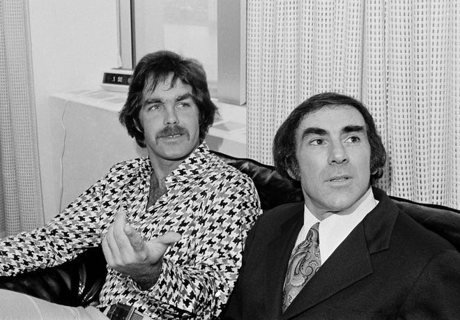 In this Feb. 7, 1973 file photo, Derek Sanderson, left, the flamboyant Boston Bruins center, meets with his attorney, Bob Woolf, in Boston after they formalized a two-year contract with the Bruins. Sanderson, who had been bought out of his five-year, $2.6 million contract by the Philadelphia Blazers of the World Hockey Assoication, had previously helped the Bruins win the 1970 Stanley Cup by accepting a supporting role. [Bill Chaplis/AP File Photo]