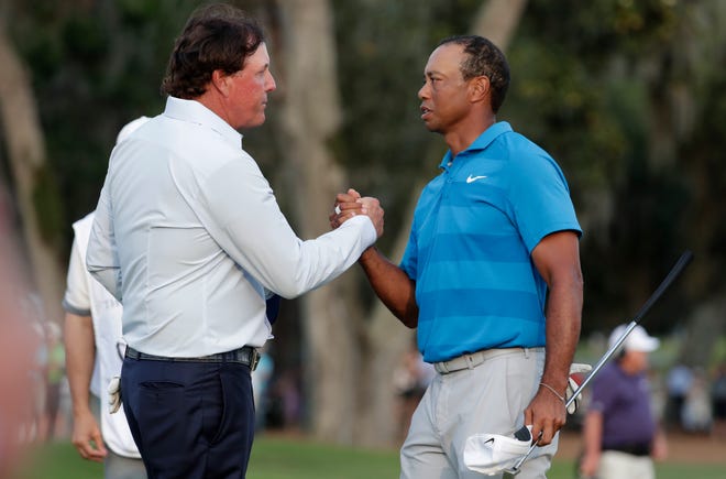 In this May 10, 2018, file photo, Phil Mickelson, left, and Tiger Woods shake hands after the first round of the Players Championship golf tournament in Ponte Vedra Beach, Fla. The PGA Tour has outlined a health plan for its return that includes players testing for the new coronavirus both at home and when they arrive at tournaments. [Lynne Sladky/AP File Photo]