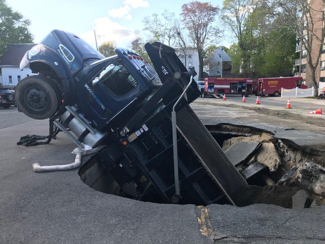 A Brockton DPW dump truck titled upward at a 45-degree angle, after dropping about 15 feet into a culvert that collapsed beneath it. [Photo by Marc Vasconcellos/Brockton Enterprise]