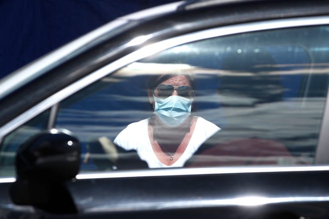 A screening worker in a mask speaks to people in a car seeking COVID-19 tests, Tuesday, April 7, 2020, in Lowell, Mass. The City of Lowell, the state and CVS Health have teamed up to open Massachusetts' first free, rapid COVID-19 drive-up testing site that will be able to test up to 1,000 people per day and provide results in about 15 minutes. (AP Photo/Elise Amendola)