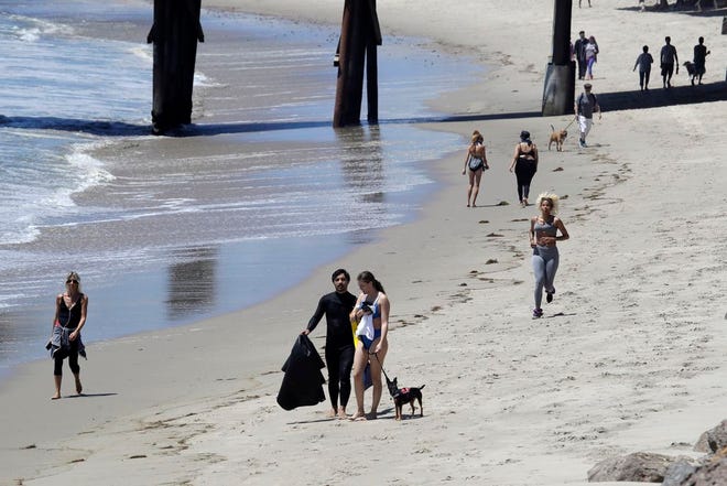 In this Wednesday, May 13, 2020, file, photo beachgoers walk and exercise on the beach in Malibu, Calif. Masks are required at Los Angeles County beaches, which reopened Wednesday to join counterparts in other states that have allowed a somewhat limited return to famed stretches of sand.