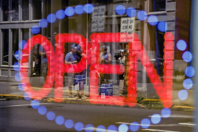 The reflection of people gathered along Butler Street in Pittsburgh’s Lawrenceville neighborhood are seen behind the “Open” sign in the window of a delicatessen as counties in southwestern Pennsylvania join northwestern and the north central regions with more relaxed COVID-19 prevention restrictions, Friday, May 15, 2020, in Pittsburgh. (AP Photo/Keith Srakocic)