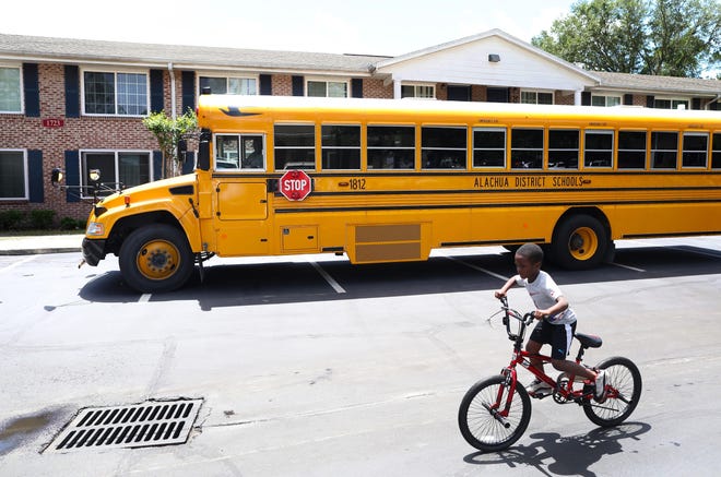 A child rides his bike past an Alachua County Public Schools bus equipped with WiFi, parked in the Gardenia Gardens Apartments in northeast Gainesville. [Brad McClenny/The Gainesville Sun]