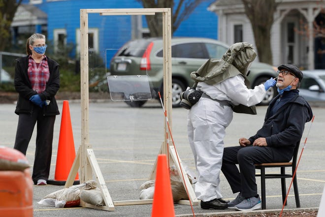 A medical worker wearing protective equipment, center, uses a swab to administer a test for the coronavirus to Chris Harkins, of Somerville, Mass., right, as his wife Gail Harkins, left, looks on, Tuesday, April 28, 2020, at a testing site in a parking lot of a hospital in Somerville, Mass. (AP Photo/Steven Senne)