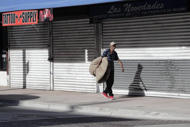 A homeless man carrying his bedding walks past shuttered businesses on May 7 in Miami. [AP Photo/Lynne Sladky]