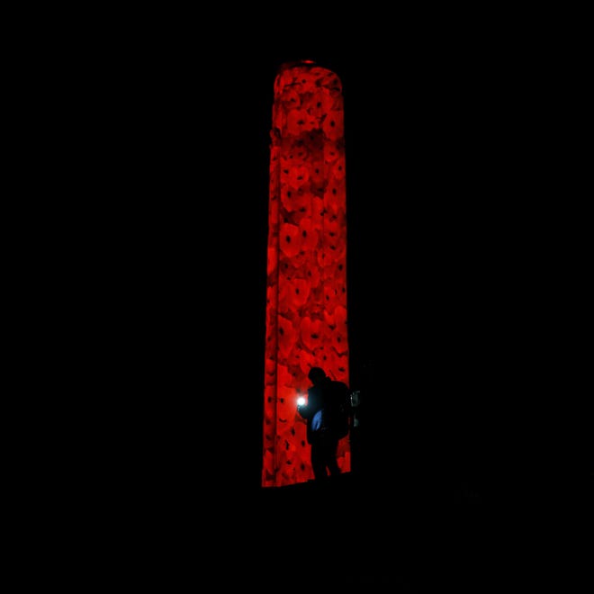 A man is silhouetted against the 217-foot-tall Liberty Memorial tower at the National World War I Museum after it was illuminated by poppies Friday, Nov. 2, 2018, in Kansas City, Mo. Red poppy flowers became a symbol of peace following World War I after they were referenced in the poem titled "In Flanders Fields." (AP Photo/Charlie Riedel)