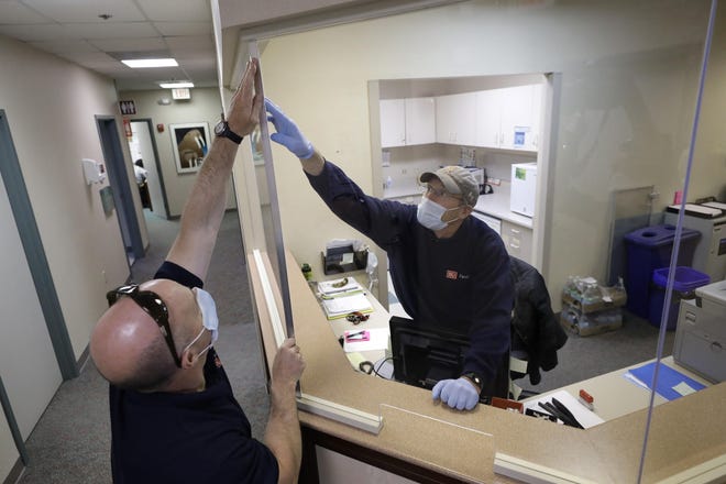 In this Wednesday, May 20, 2020 photo carpenters John Mackie, of Canton, Mass., left, and Doug Hathaway, of Holliston, Mass., right, apply trim to a newly installed plastic barrier in an office area, at Boston University, in Boston. Boston University is among a growing number of universities making plans to bring students back to campus this fall, but with new measures meant to keep the coronavirus at bay. (AP Photo/Steven Senne)