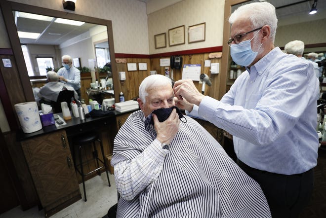 FILE - In this May 15, 2020 file photo, barber Lannie Hale cuts Bob Mitchell's hair at his Waveland Barber Stylist shop in Des Moines, Iowa. With more businesses across the country easing back to life, the new challenge will be how to keep workers safe during the pandemic. From temperature checks, contact tracing, social distancing and staggered schedules, a variety of new protocols are being implemented. (AP Photo/Charlie Neibergall)