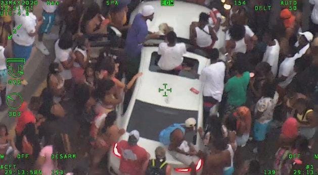 A screen capture from Volusia County Sheriff's Office helicopter video showing a crowd around a white car on Atlantic Avenue Saturday. Hundreds of people crowded the Boardwalk area for a party advertised with the slogan “invade Daytona.”