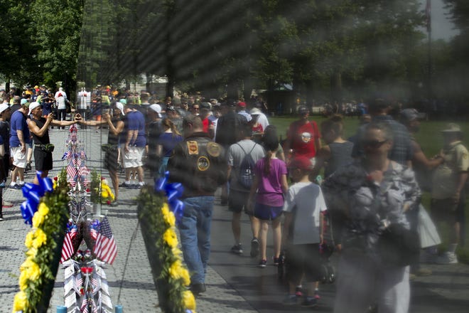 Visitors are reflected on the Vietnam Veterans Memorial wall in Washington, D.C. The wall contains about 58,000 names — 45,000 fewer than have died from COVID-19 in just four months. [Jose Luis Magana/Associated Press]