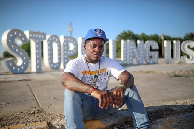 Jabee Williams poses with a large illuminated sign reading "Stop killing us," part of efforts aimed at bringing attention to police shootings.