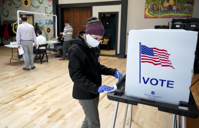 Shanon Hankin cleans a voter booth after it was used for voting at the Wil-Mar Neighborhood Center Tuesday, April 7, 2020 in Madison, Wis. [STEVE APPS/WISCONSIN STATE JOURNAL VIA AP]