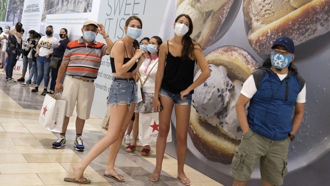 Shoppers with masks wait to ender a store at a mall in Paramus, N.J. [Associated Press Photo]