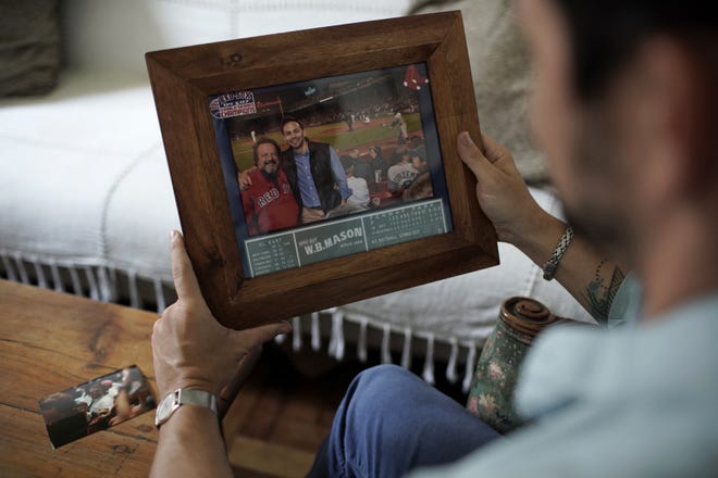 David Biller holds a photo of himself and his father on Friday, Sept. 18, 2020, at his apartment in Rio de Janeiro, Brazil. The photo is from when they watched the Red Sox beat the Yankees in the bottom of the ninth inning on Sept. 11, 2012, at Fenway Park, in Boston. One month later, the author moved to Brazil. (AP Photo/Silvia Izquierdo)