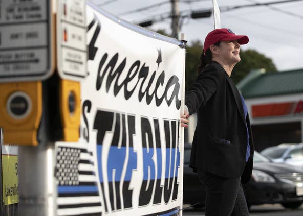 A woman holds a sign reading America Backs the Blue and signs for President Donald Trump at the We Back the Blue rally organized by the Middleborough Republican Town Committee at the intersection of Route 28 and Route 105 in Middleboro on Monday, Sept. 28, 2020. [Alyssa Stone/The Enterprise]