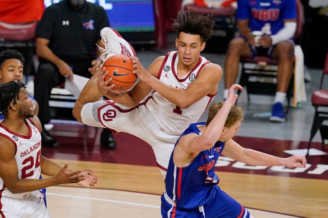 Oklahoma forward Jalen Hill, top, catches the ball and lands on Houston Baptist guard Hunter Janacek, right, in the first half of an NCAA college basketball game Saturday, Dec. 19, 2020, in Norman, Okla. (AP Photo/Sue Ogrocki)
