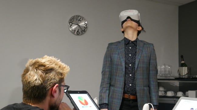 Landon Whitt, CEO of OKCReal, watches a tablet to make sure the signal is staying strong during the 10-second collection of brain activity when the viewer first enters the virtual reality space, while Sara Abolhosn looks up while wearing the headset to see how tall the ceiling was in the home she was touring. [PROVIDED/OKCREAL]