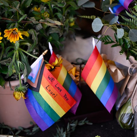 Rows of flowers and pride flags cover the Mag Pi storefront window as a memorial for store owner Laura Ann 