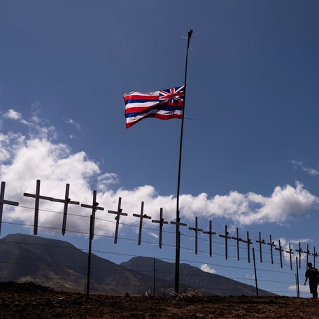 Crosses honoring the victims killed in a recent wildfire hang on a fence along the Lahaina Bypass as a Hawaiian flag flutters in the wind in Lahaina, Hawaii, Tuesday, Aug. 22, 2023. (AP Photo/Jae C. Hong) ORG XMIT: HIJH101
