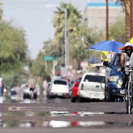 A person rides a bicycle as heat waves shimmer, causing visual distortion, as people walk in the 'The Zone', Phoenix's largest homeless encampment, amid the city's worst heat wave on record on July 25, 2023 in Phoenix, Arizona. While Phoenix endures periods of extreme heat every year, today is predicted to mark the 26th straight day of temperatures reaching 110 degrees or higher.